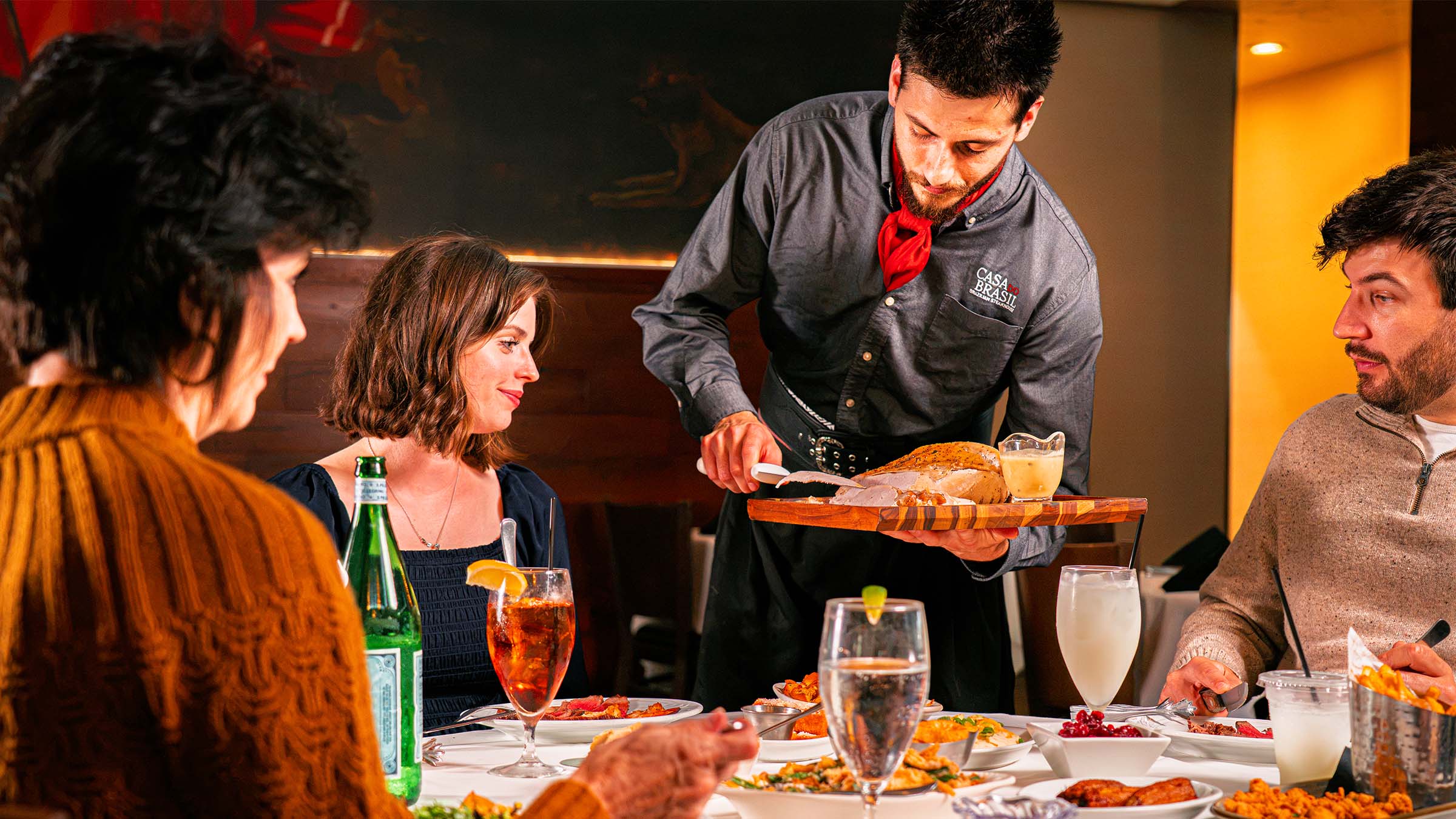 A gaucho chef serves turkey tableside to a family gathered for Thanksgiving at Casa do Brasil
